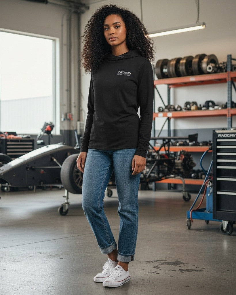 Woman wearing a black Crown Speed Shop Ultra hooded long sleeve shirt with blue jeans in an automotive garage.