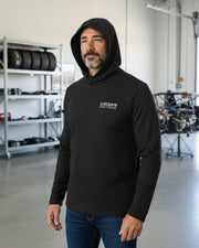Man wearing a black Crown Speed Shop UNRL Ultra hooded long sleeve shirt in a garage setting